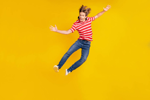 Photo of funny excited young man wear striped t-shirt smiling jumping high isolated yellow color background - Фото, зображення
