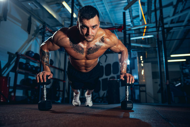 Fronr view of muscled athlete, bodybuilder workouts alone at sport gym, indoors. Concept of sport, activity, healthy lifestyle - Fotografie, Obrázek
