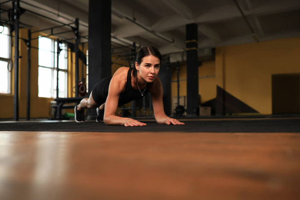 Portrait of a muscular woman on a plank position - Foto, afbeelding