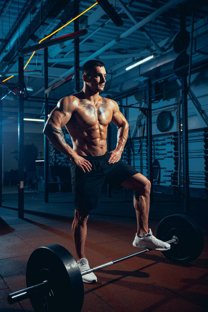 Young strong man, muscled athlete, bodybuilder training alone at sport gym, indoors. Concept of sport, activity, healthy lifestyle - 写真・画像