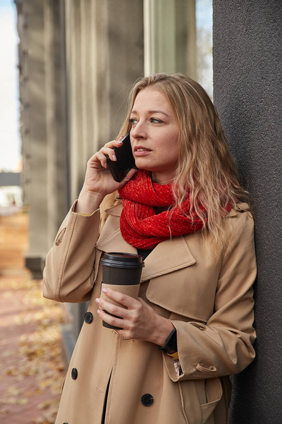 kavkazská žena v béžovém plášti volá smartphone s šálkem kávy - Fotografie, Obrázek