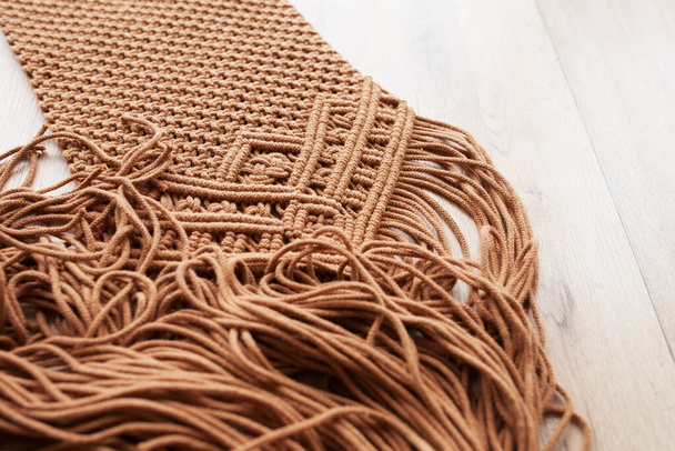 Handmade macrame pattern close up. Macrame braiding and cotton threads on wooden table.  Female hobby.  ECO friendly modern knitting DIY natural decoration concept in the interior. Copy space - 写真・画像