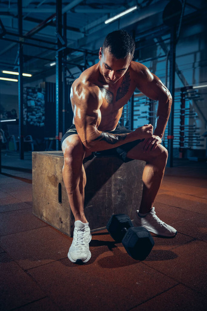 Image of young man, bodybuilder training with dumbbells at modern sport gym, indoors. Concept of sport, activity, healthy lifestyle - Fotó, kép