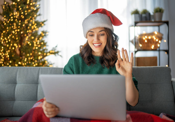 Woman is chatting using laptop in the living room decorated for Christmas. - Zdjęcie, obraz