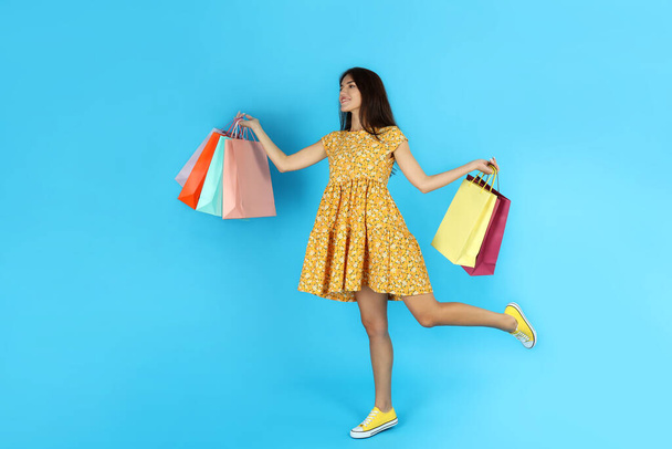 Attractive girl with multicolored paper bags on blue background. - Foto, afbeelding