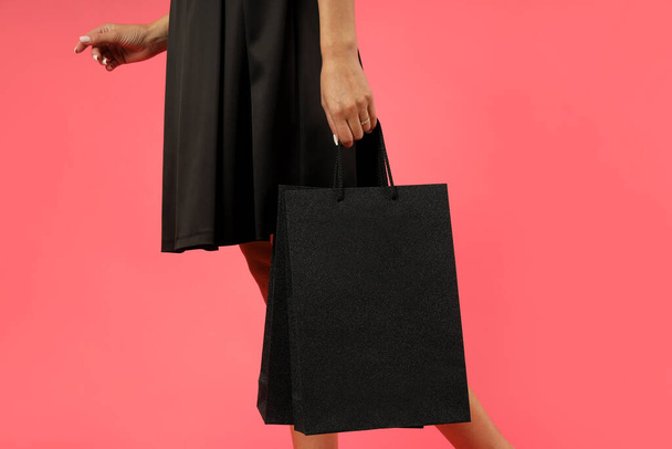 Привлекательная девушка в черном платье с бумажными пакетами на розовом фоне. - Фото, изображение
