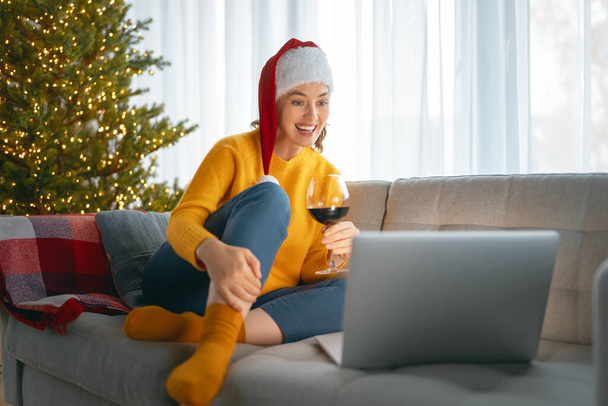Woman is chatting using laptop in the living room decorated for Christmas. - Foto, Imagem
