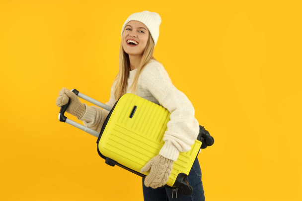 Attractive girl in winter clothes with luggage bag on yellow background. - Fotó, kép
