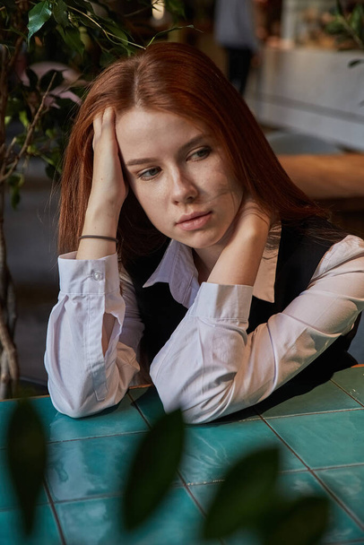 Kafkasyalı kızıl saçlı, uzun saçlı güzel kız kahve masasında oturuyor. - Fotoğraf, Görsel