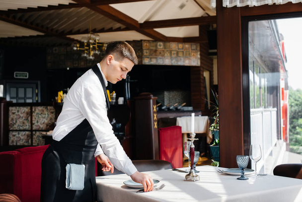 A young male waiter in a stylish uniform is engaged in serving the table in a beautiful gourmet restaurant. Restaurant activity, of the highest level. - Foto, immagini