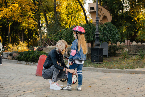 Mom helps dress up her little daughter's gear and helmet for a Segway ride in the Park. Happy family vacation. - Foto, afbeelding