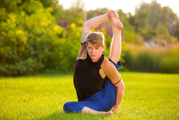 A very flexible young man doing yoga on the lawn at sunset - Foto, immagini