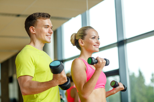 smiling man and woman with dumbbells in gym - Foto, imagen