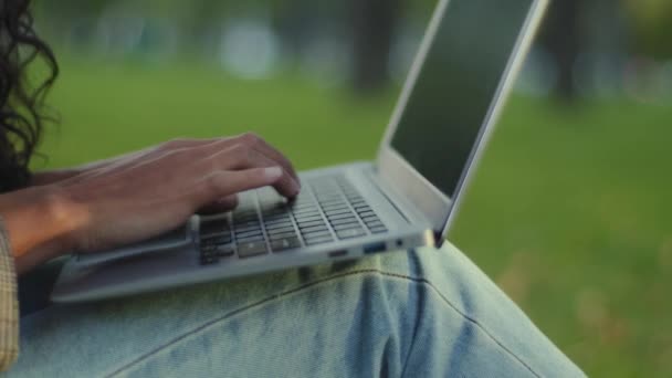 Close-up kobiet ręce palce wpisując na klawiaturze klawiatury laptop tekst komputerowy pracy uczenia się e-learning na świeżym powietrzu w parku. Nierozpoznawalna dziewczyna brunetka kobieta w dżinsach siedzi na trawniku na czacie online - Materiał filmowy, wideo