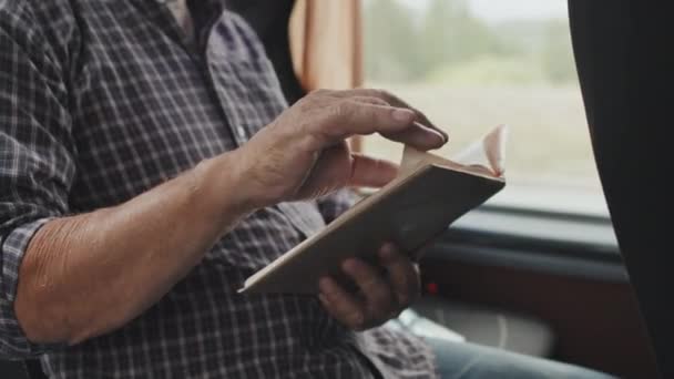 Środek kadru nierozpoznawalnego starszego mężczyzny w koszuli w kratkę, siedzącego przy oknie czytającego książkę z papieru podczas jazdy autobusem - Materiał filmowy, wideo