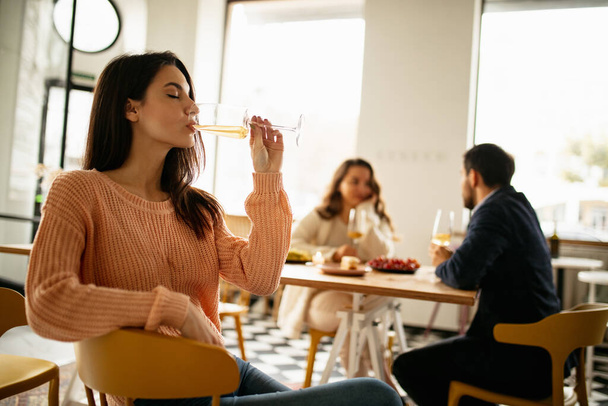 Обрезанный портрет красивой женщины, пьющей белое вино, празднующей событие с кормильцами в кафе в теплый солнечный день - Фото, изображение