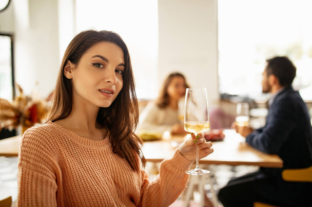 Ausgeschnittenes Porträt einer schönen Frau, die Weißwein trinkt und an warmen, sonnigen Tagen eine Feier mit Handgelenken im Café feiert - Foto, Bild