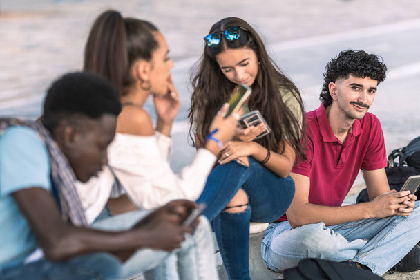 Homem moderno caucasiano sentado ao lado de grupo diversificado de amigos usando o celular - Foto, Imagem