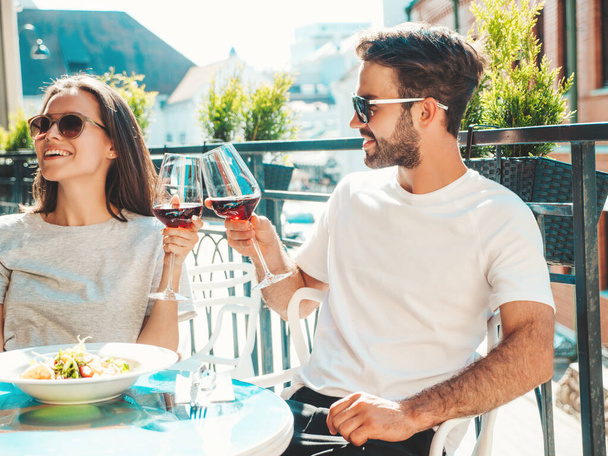 Smiling beautiful woman and her handsome boyfriend. Happy cheerful family. Couple cheering with glasses of red wine at their datein restaurant. They drinking alcohol at veranda cafe in the street - Foto, Imagen