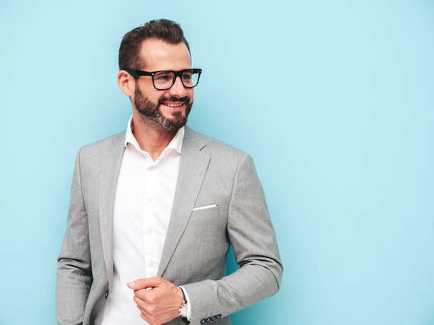 Portrait of handsome smiling stylish hipster lambersexual model.Sexy modern man dressed in elegant suit and spectacles. Fashion male posing in studio near blue wall. Looking at camera in glasses - Φωτογραφία, εικόνα