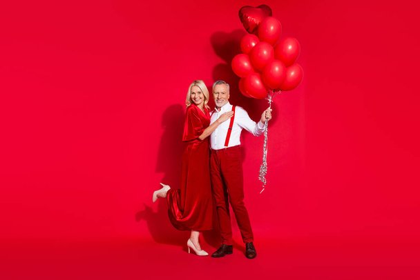 Full size photo of retired girlfriend boyfriend romantic cuddle feelings many air balls suspenders isolated over red color background - Foto, Imagem