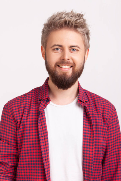 Portrait of cheerful bearded young adult male in plaid shirt sincerely smiling looking at camera, optimistic lifestyle. Indoor studio shot isolated on gray background - Zdjęcie, obraz