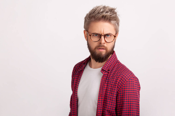 Portrait of puzzled blond bearded man wearing eyeglasses frowning and seriously looking at camera. Indoor studio shot isolated on gray background - Photo, Image