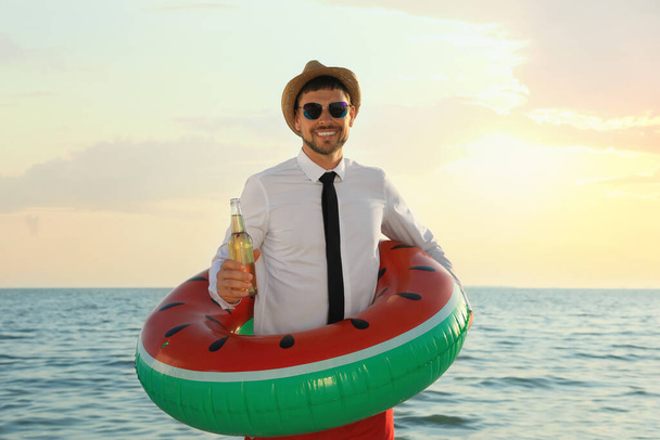 Happy man with inflatable ring and beer on beach. Business trip - Fotoğraf, Görsel