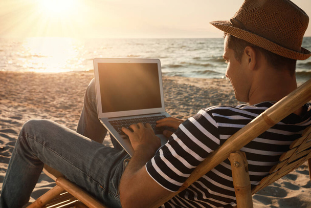 Man working with laptop in deck chair on beach - Foto, afbeelding