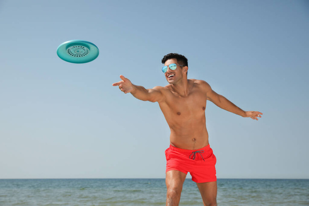 Happy man throwing flying disk at beach on sunny day - Фото, зображення