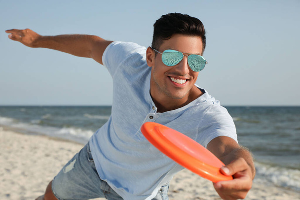 Happy man throwing flying disk at beach on sunny day - Fotoğraf, Görsel