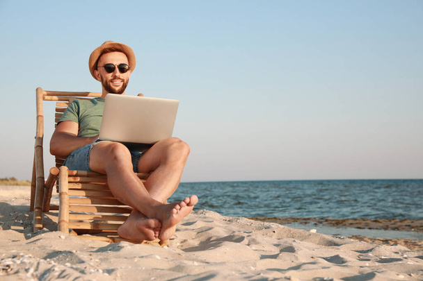 Man working with laptop in deck chair on beach. Space for text - Photo, image