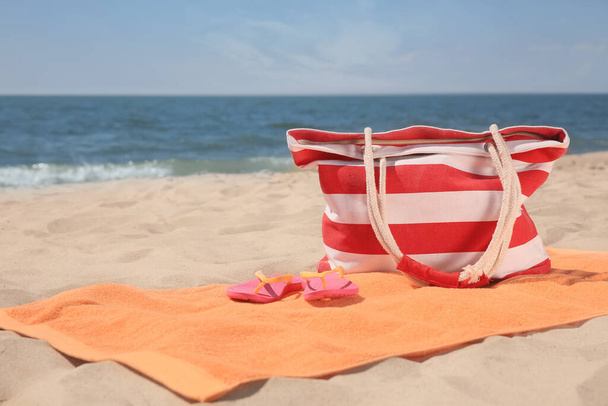 Soft orange beach towel, bag and flip flops on sandy seashore, space for text - Photo, image