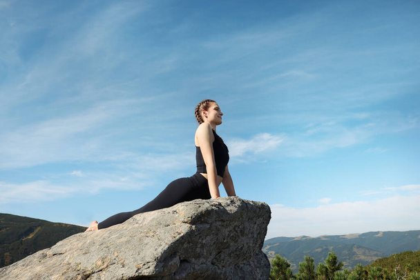 Beautiful young woman practicing yoga on rock in mountains - Photo, image