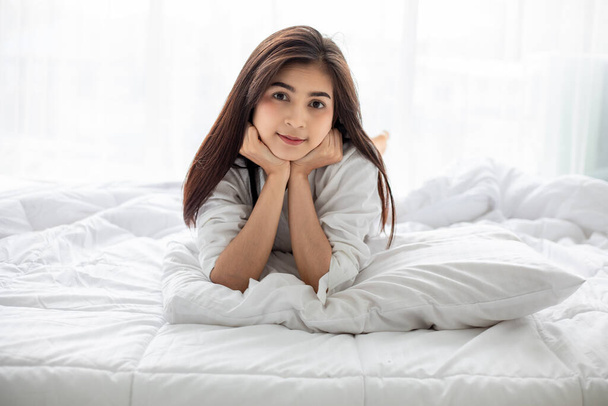 Donna asiatica Bella giovane donna sorridente seduta e addormentata nel letto bianco e che si estende al mattino in camera da letto dopo essersi svegliata nel suo letto completamente riposata - Foto, immagini