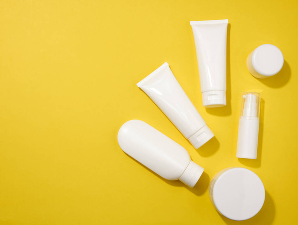 jar, bottle and empty white plastic tubes for cosmetics on a yellow background. Packaging for cream, gel, serum, advertising and product promotion, mock up - Φωτογραφία, εικόνα