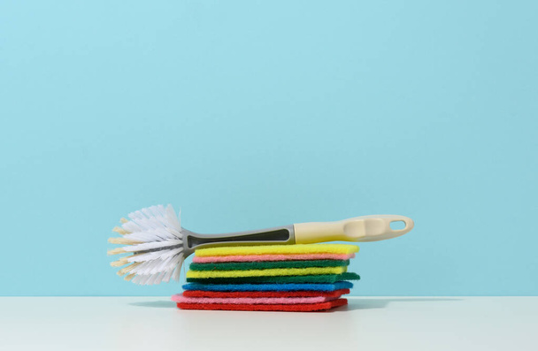 esponja y cepillo de plástico con asa para limpiar la casa sobre un fondo azul - Foto, imagen