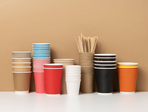 pile di tazze di carta usa e getta assortiti per bevande, caffè e tè su un tavolo bianco. Contenitore per bevande da asporto - Foto, immagini