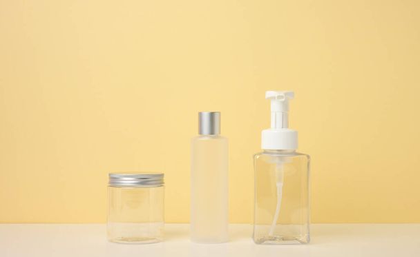 tubos crema, dispensador cosmético, frasco de plástico vacío, dispensador transparente sobre un fondo amarillo claro. Branding de productos cosméticos, maqueta - Foto, imagen