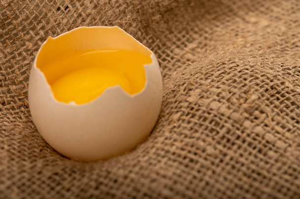 Um ovo de galinha branco quebrado em um tecido caseiro com uma textura áspera, foco seletivo close-up - Foto, Imagem