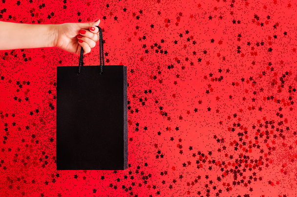 the concept of black friday. black bag in hand on a red background with space for text - Photo, Image