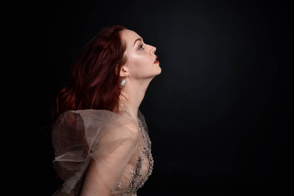 close up portrait of red haired  girl wearing a creamy fantasy gown like a fairy goddess costume.  isolated on dark studio background. - Foto, Bild