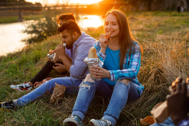 The group of young diverse people eating fastfood on nature - Foto, afbeelding