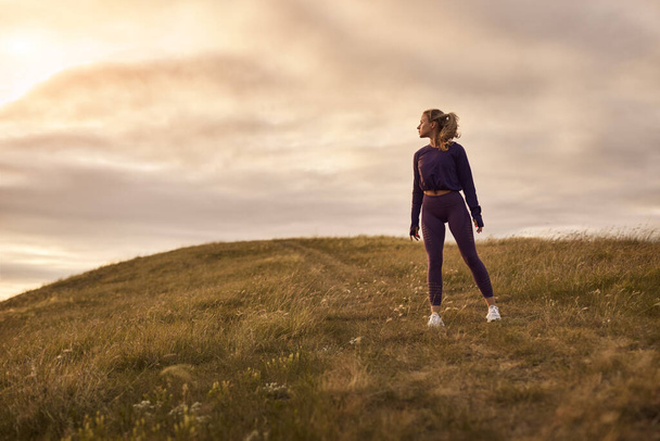 Sportswoman standing on hill in sunset - Foto, afbeelding
