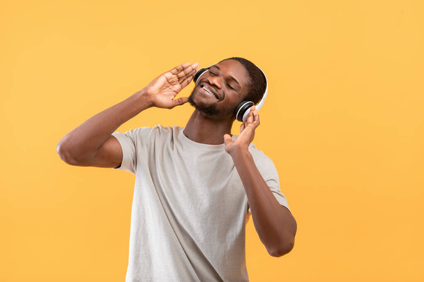 Η καλύτερη μουσική. Χαρούμενος Αφροαμερικάνος με ασύρματα ακουστικά απολαμβάνοντας τα αγαπημένα του τραγούδια και χαμογελώντας - Φωτογραφία, εικόνα