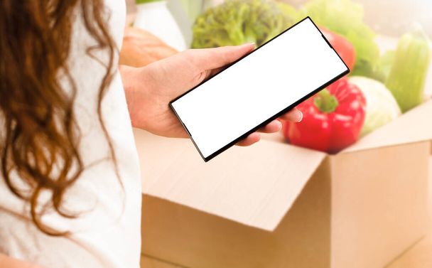 woman holds phone in hand with copy space. home delivery, grocery ordering, order collection - Photo, Image