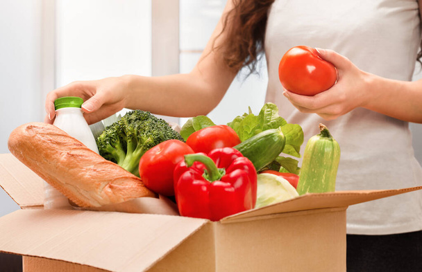 mujer saca comida fresca de la caja, entrega a domicilio, desembalaje de productos - Foto, imagen