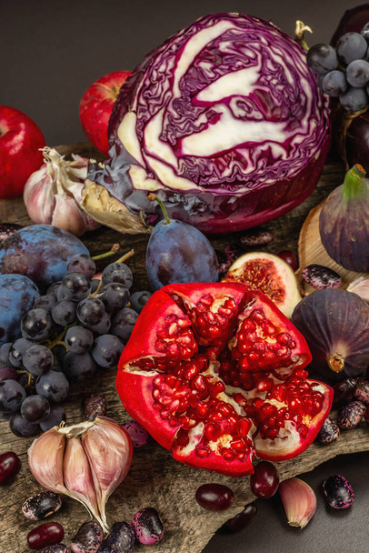 Niebieskie, czerwone i fioletowe jedzenie. Kulinarne tło owoców i warzyw. Świeże figi, śliwki, cebula, bakłażan, winogrona, kapusta, jabłka, czosnek, piesek, granat. Czarny kamień tło, płaski leżak - Zdjęcie, obraz