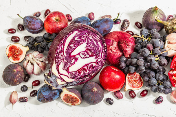青、赤、紫の食品。果物や野菜の料理の背景。新鮮なイチジク、プラム、玉ねぎ、ナス、ブドウ、キャベツ、リンゴ、ニンニク、ドッグウッド、ザクロ。白い背景、流行のハードライト - 写真・画像