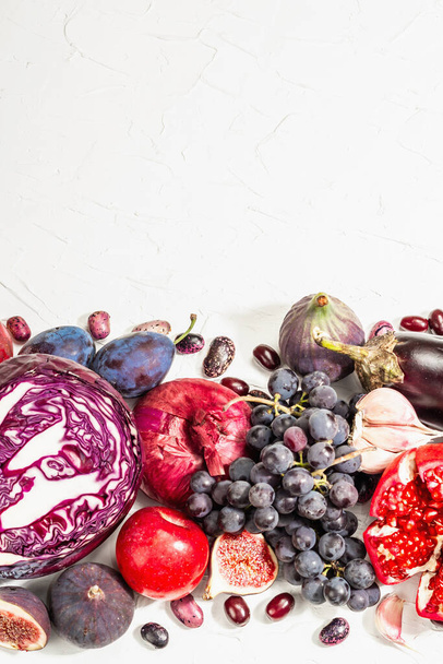 Blue, red and purple food. Culinary background of fruits and vegetables. Fresh figs, plums, onions, eggplant, grapes, cabbage, apples, garlic, dogwood, pomegranate. White background, trendy hard light - Photo, Image